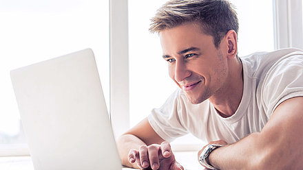 WLAN-Optimierung auf Knopfdruck – automatisiert und selbstlernend, mit LANCOM Active Radio Control™ 2.0 Glücklich-entspannter junger Mann beobachtet erfreut die Auswirkungen seines optimierten WLANs auf seinem Laptop